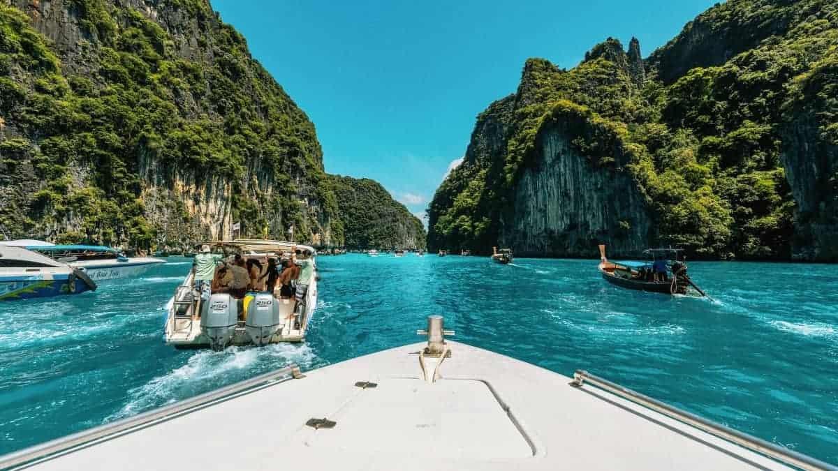 Een uitzicht vanaf een boot die door helder turquoise water vaart omringd door hoge, weelderige groene kliffen, met verschillende andere boten en speedboten in de buurt onder een helderblauwe hemel.