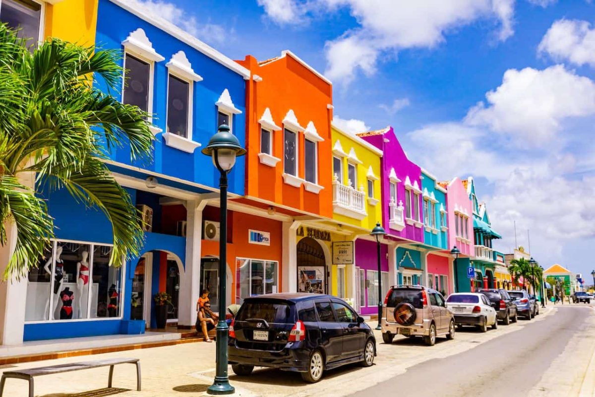 Experience the vibrant sights of Bonaire on the Private Island and Snorkel Tour, where rows of bright blue, orange, yellow, pink, and green buildings line sunny streets lined with palm trees and picturesque skies.