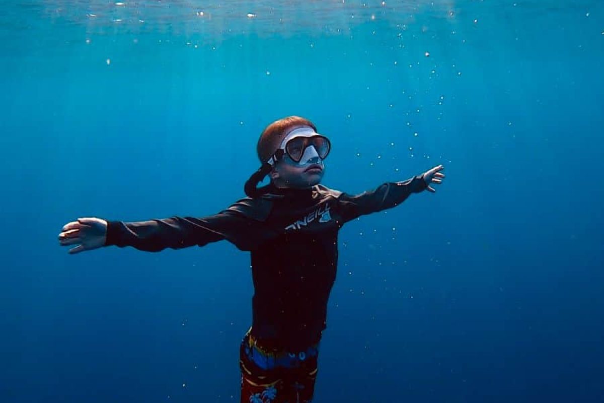 Con equipo de snorkel y aletas puestas, alguien flota bajo el agua bajo la superficie bañada por el sol de Bonaire; vivid esto con el Curso de Buceo Libre para Principiantes. Los rayos de sol atraviesan las claras aguas azules sobre ellos mientras exploran.