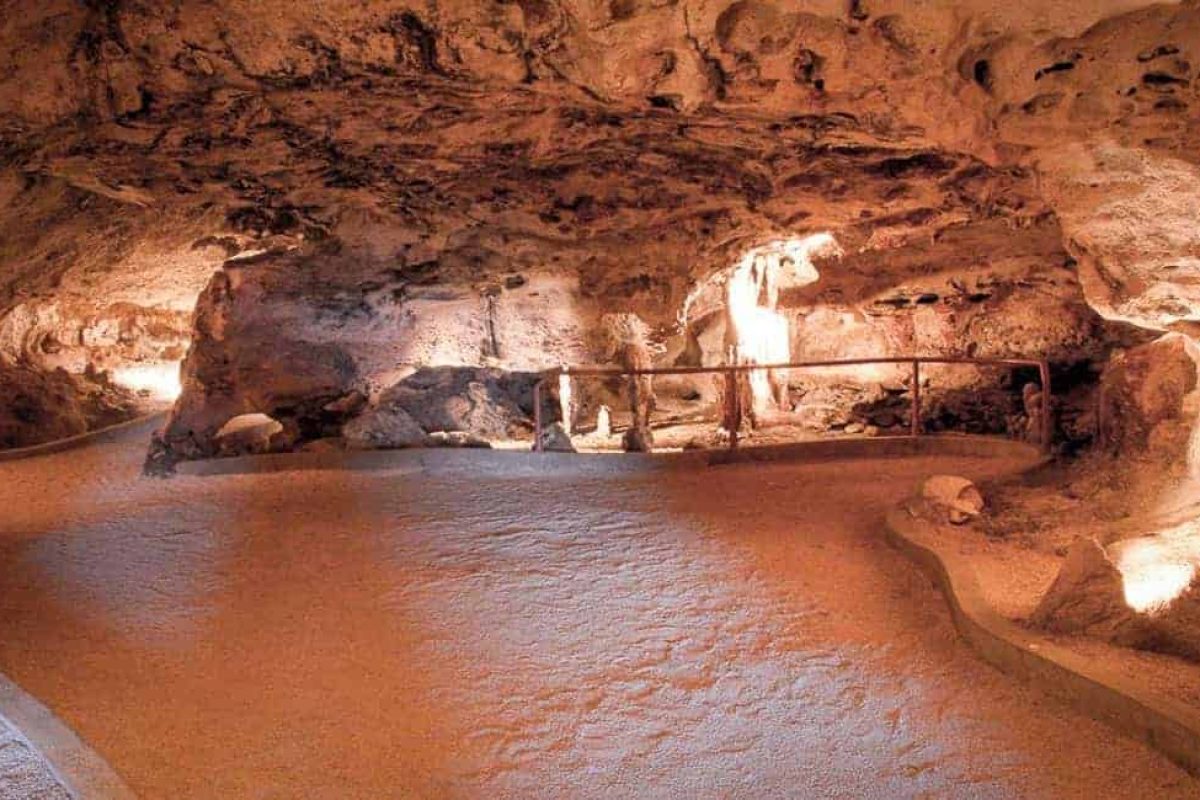 Explora el interior bien iluminado de la Cueva Hato con paredes rocosas texturizadas, suelo arenoso y un sendero bordeado por barandillas en la Willemstad: Cueva Hato, Flamencos y Turtle Beach Tour (Curazao).