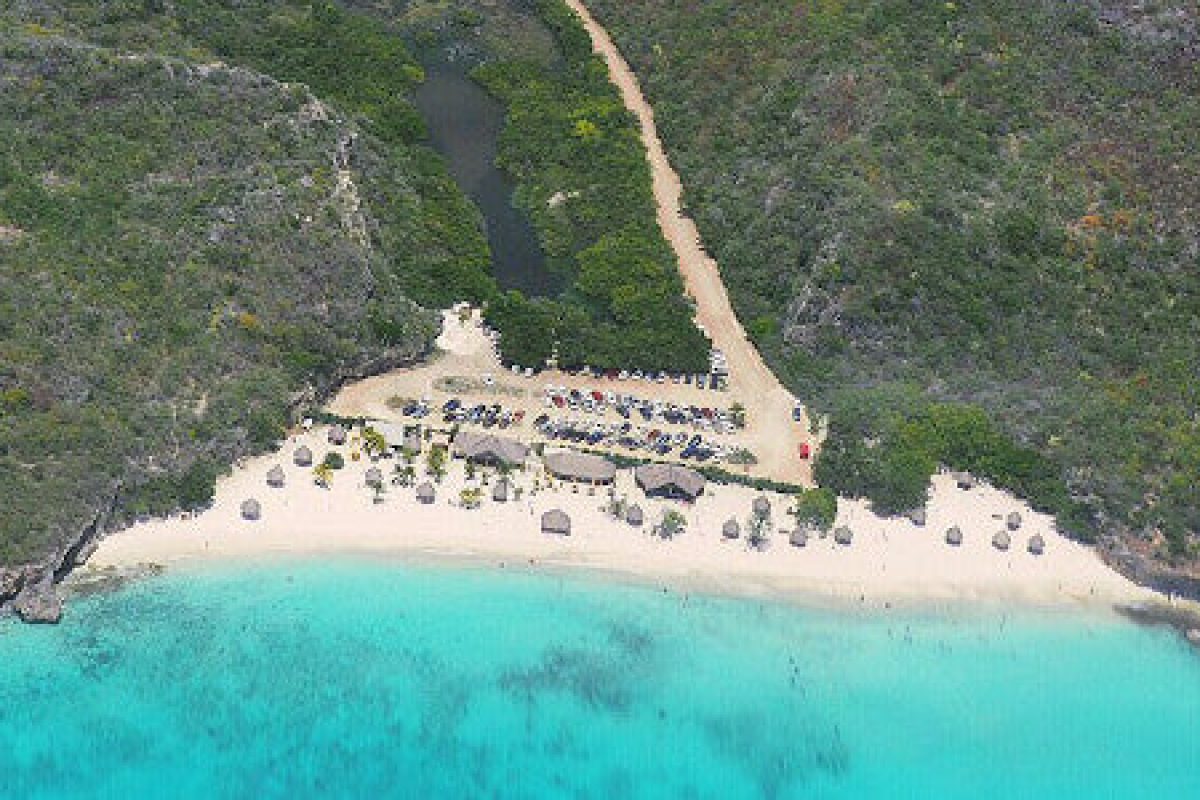 Luchtfoto van het Snorkel en strandavontuur van Curaçao: turquoise water, wit zand, ligstoelen, parasols en weelderige groene vegetatie met een pad dat van het strand naar het tropische gebladerte leidt.