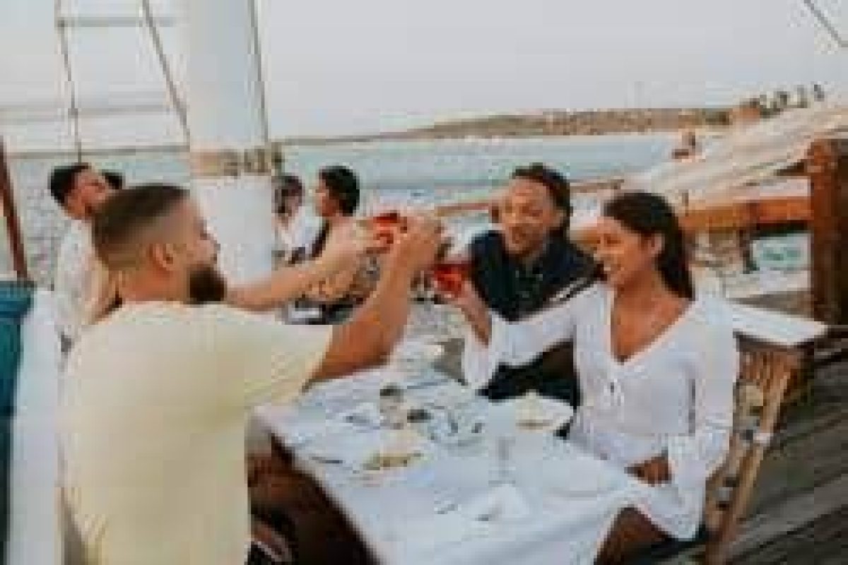 Un grupo de personas brinda y se ríe en la mesa de un barco durante el Sunset Cruise con una cena de cuatro platos (Aruba), con vistas al océano y a la costa lejana.