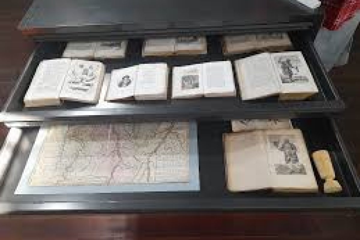 La excursión de un día Plantation Bakkie Commewijne cuenta con tres vitrinas con libros antiguos, papeles antiguos y un mapa antiguo. Los libros ilustrados muestran material impreso histórico en un entorno similar a un museo.