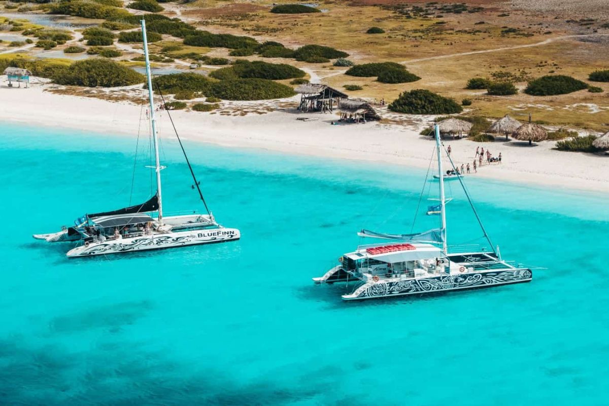 Vista aérea de dos catamaranes con patrón anclados en aguas claras cerca de una playa de arena con arbustos verdes y chozas, parte del tour 3 en 1 Snorktocht (Curazao).